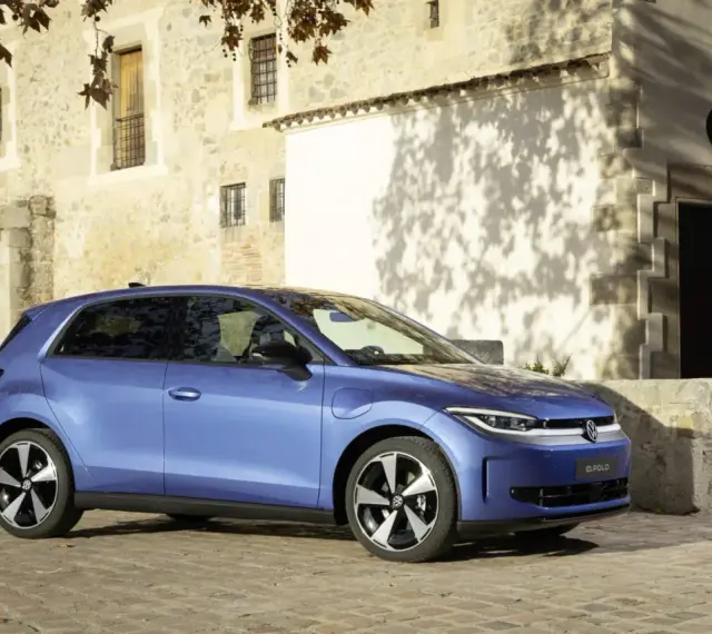 Niebieski samochód elektryczny VW ID. Polo stoi na brukowanej drodze przed kamiennym budynkiem.