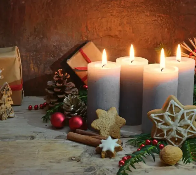 Vier brennende Kerzen im **Hintergrund Adventszeit**, umgeben von Tannenzweigen, Geschenken, Nüssen und Weihnachtsplätzchen.