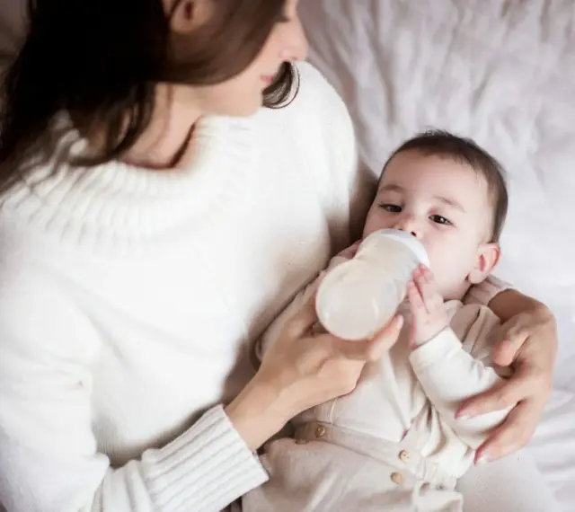 Mama karmi butelką dziecko, które właśnie pije mleko. Ważne jest, ile mleka powinien jeść noworodek.
