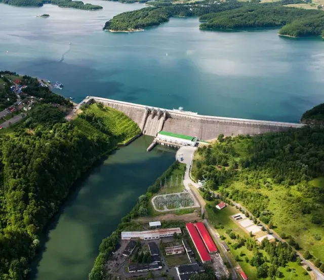 Zapora Solina z lotu ptaka, otoczona zielonymi wzgórzami i błękitną wodą. Planujesz wycieczkę? Sprawdź zapora Solina bilety!