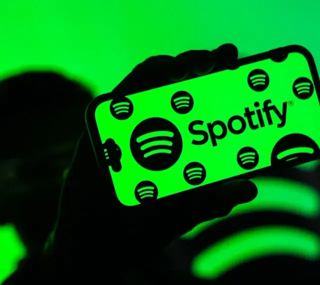 Dłoń trzyma smartfon z zielonym ekranem, na którym widnieje logo Spotify. Użytkownik cieszy się doskonałą spotify jakość dźwięku.
