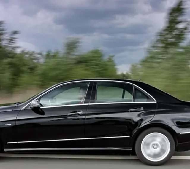 Czarny Mercedes E350 pędzi po drodze, mijając rozmyte zielone drzewa.