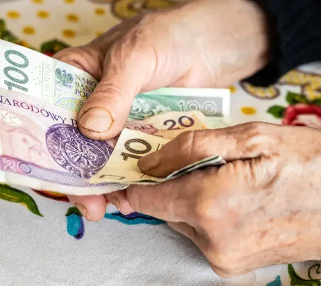 Dłonie starszej osoby liczą pieniądze. Może to być dodatek opiekuńczy po 80 roku życia, zapewniający wsparcie finansowe.