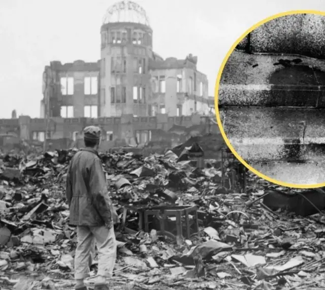 Ruiny w Hiroszimie po bombardowaniu atomowym. W oddali widać zniszczony budynek, a na pierwszym planie stos gruzów i stojącego człowieka. W kółku widoczny ślad po ciele.