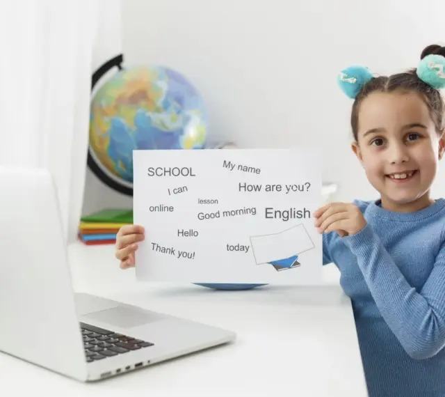 Uśmiechnięta 6latka z tabliczką "English" i zwrotami do nauki. Obok laptop i globus.