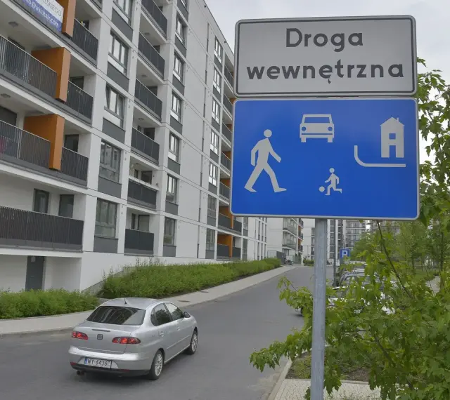 Droga wewnętrzna w terenie zabudowanym. Znak informuje o ruchu pieszych, samochodów i domów.