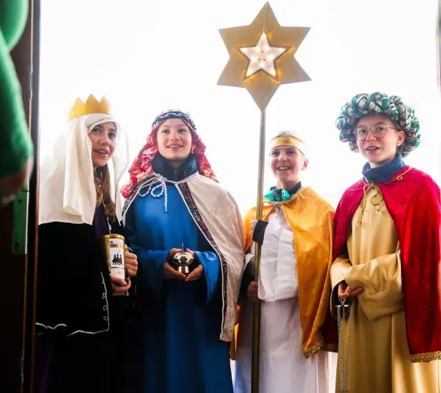 Vier Kinder als Sternsinger evangelisch verkleidet, mit Stern und Spendenbüchse, stehen vor einer Tür.