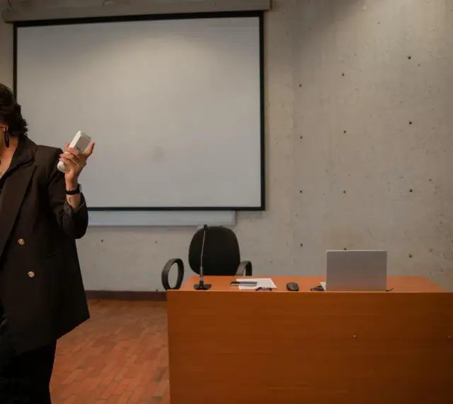 En kvinna håller mikrofon och en fjärrkontroll, redo att presentera en tes.