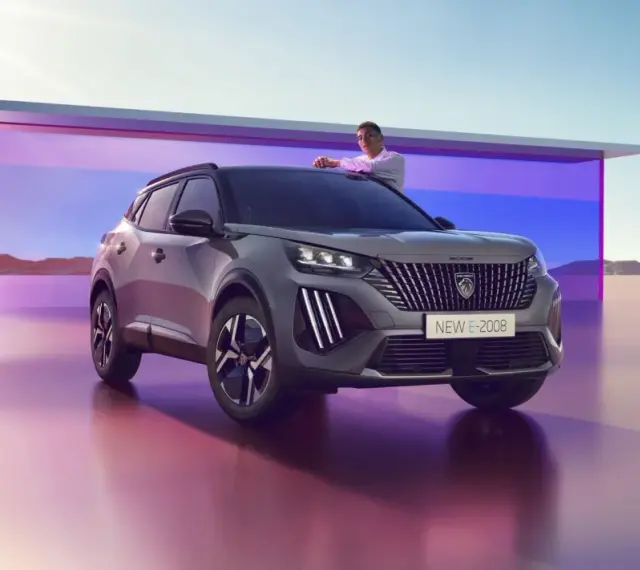 Mężczyzna opiera się o maskę nowego Peugeot E-2008, stylowego peugeot suv, na tle futurystycznej architektury i pustynnego krajobrazu.