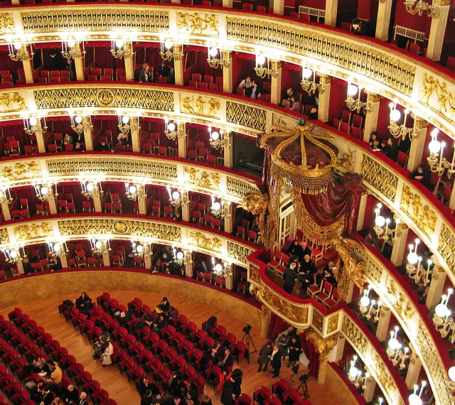 Elegancka loża w teatrze, z czerwonymi aksamitnymi siedzeniami i złotymi zdobieniami, czeka na widzów.