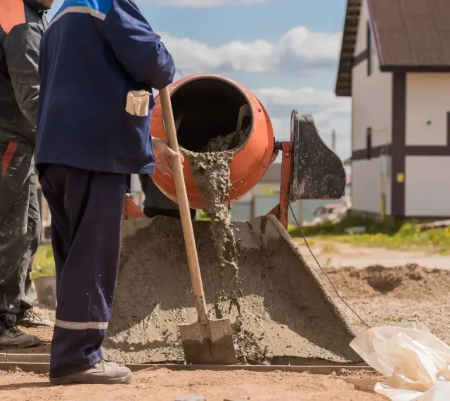 Dwóch budowlańców miesza beton. Zastanawiamy się, ile łopat żwiru na worek cementu, by uzyskać idealną konsystencję.