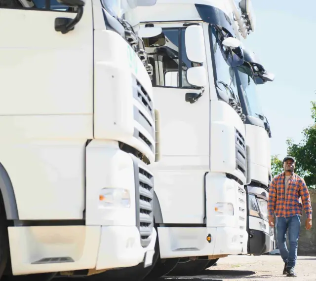 Kierowca idzie obok rzędu białych ciężarówek. To właśnie spedycja co to – transport towarów na dużą skalę.