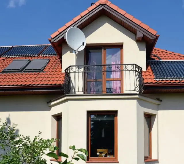 Elegancki wykusz w domu z balkonem i anteną satelitarną. Na dachu widoczne kolektory słoneczne.