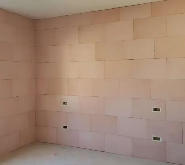 Pannelli rosa per cappotto interno con lana di roccia e cartongesso, con predisposizioni per prese elettriche e una finestra.