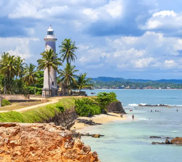 Latarnia morska na Sri Lance, otoczona palmami, z widokiem na ocean i plażę. Idealne miejsce na wakacje, warto sprawdzić wizę Sri Lanka.