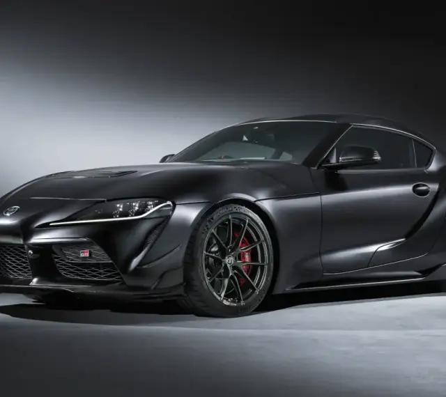 Matowa czerń podkreśla agresywną sylwetkę sportowego coupe Toyota GR Supra. Widoczne czerwone zaciski hamulcowe i aerodynamiczne dodatki.