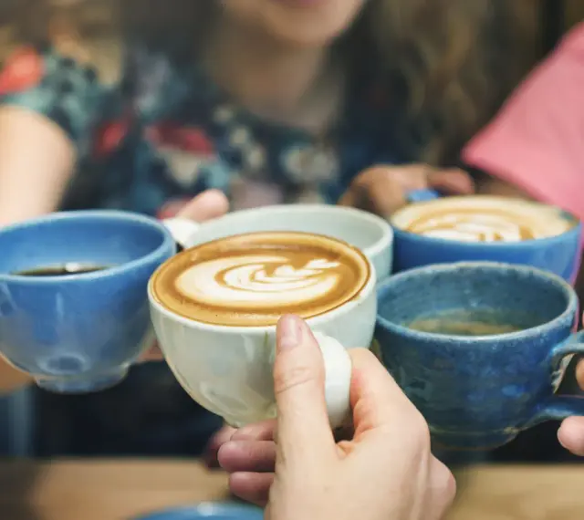 Vier Hände halten bunte Kaffeetassen. Der Kaffee reizt die Blase, aber der Genuss ist es wert.