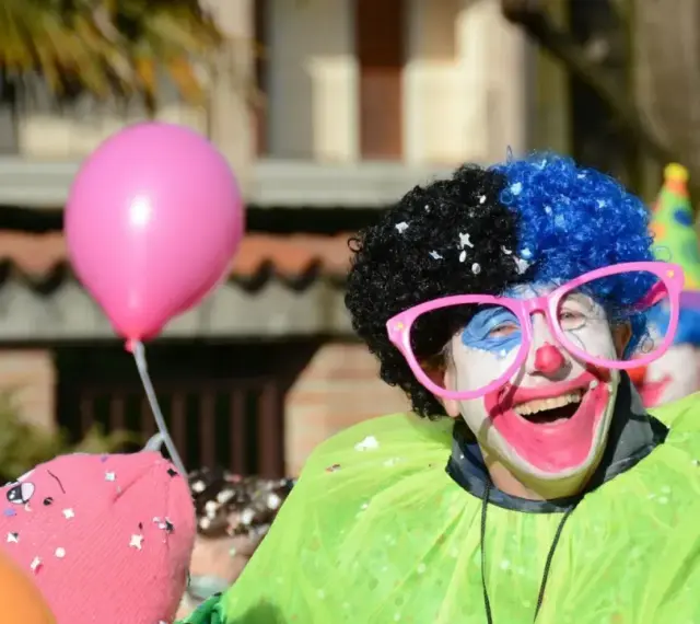 Uśmiechnięty animator w peruce i okularach, otoczony balonami, przygotowuje się do zabawy.