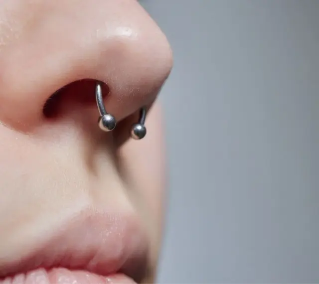 Zbliżenie na nos z kolczykiem typu septril piercing. Metalowy okrąg z dwoma kulkami subtelnie zdobi przegrodę nosową.