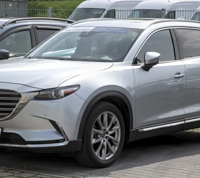 Srebrna Mazda CX-9 z napisem "PRE-OWNED" na przedniej szybie, zaparkowana na zewnątrz.