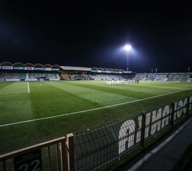 Piłkarze na murawie stadionu Górnik Łęczna, oświetlonego jupiterami.
