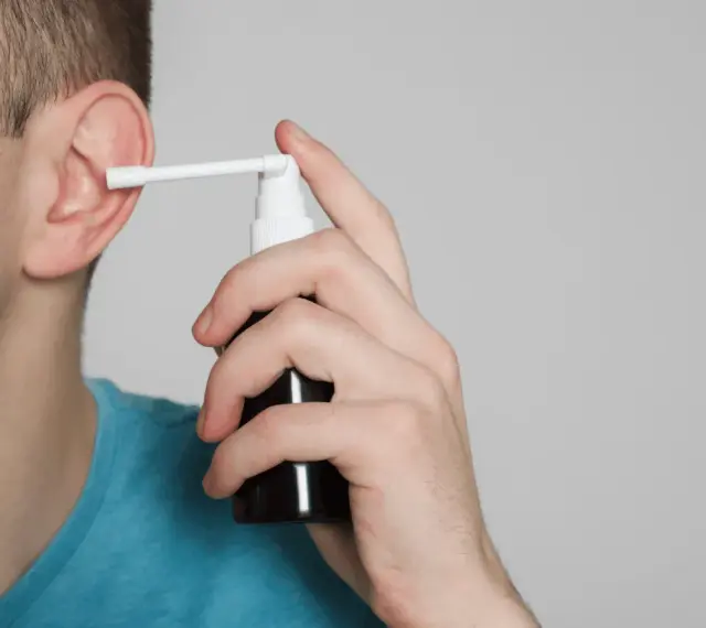 Mężczyzna aplikuje spray do ucha, łagodząc płyn w komórkach wyrostka sutkowatego.