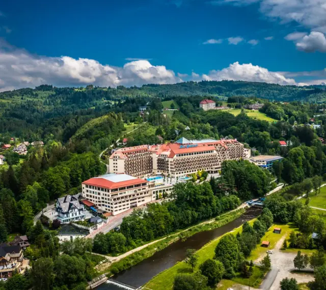 Widok z lotu ptaka na Hotel Gołębiewski w otoczeniu zielonych wzgórz i rzeki.