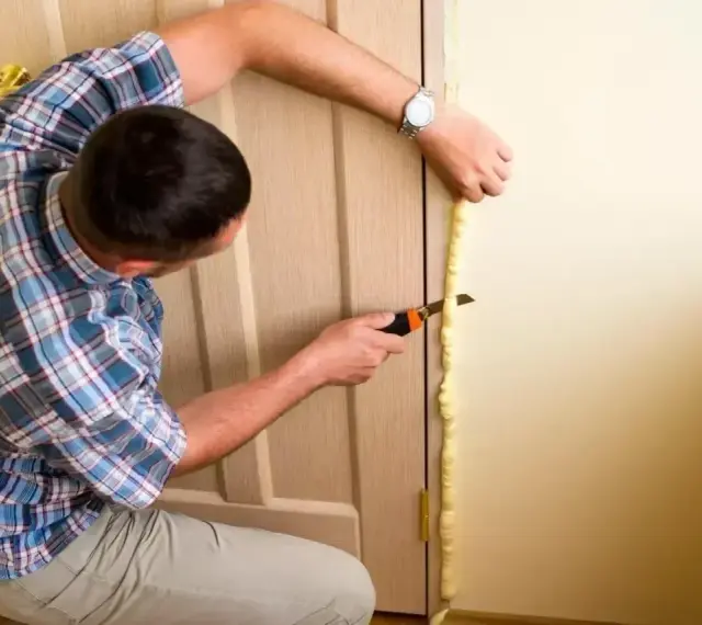 Montaż drzwi wewnętrznych cena: fachowiec docina piankę montażową wokół ościeżnicy.