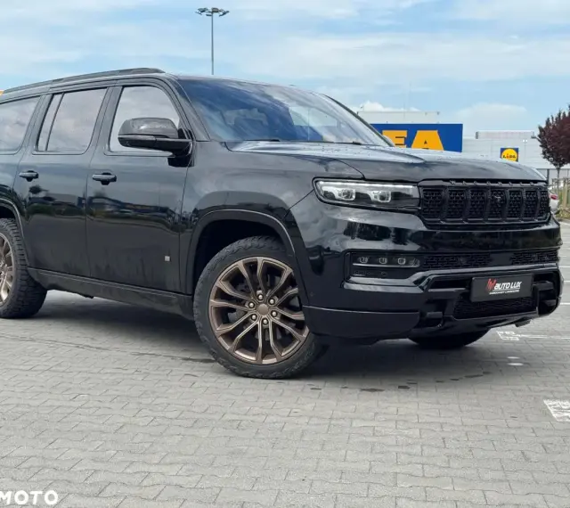 Czarny Grand Wagoneer z brązowymi felgami stoi na parkingu przed sklepami.