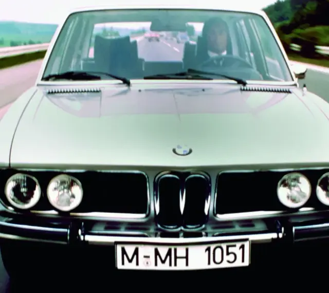 Srebrne BMW E3 z lat 70. jedzie po drodze.