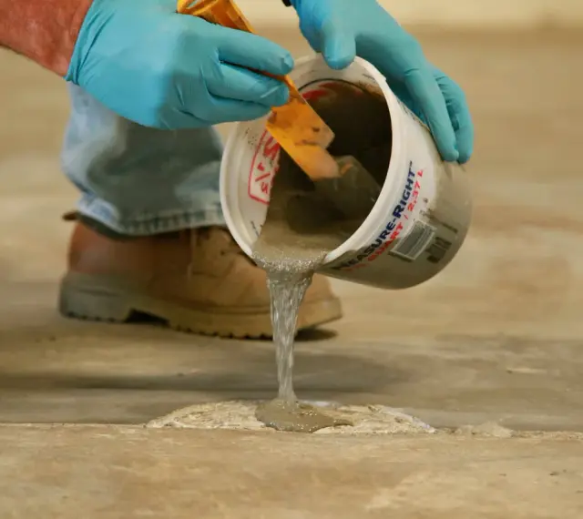 Man con guantes azules vierte hormigón líquido de un cubo para reparar el suelo. Aprende como hacer hormigón para suelo.
