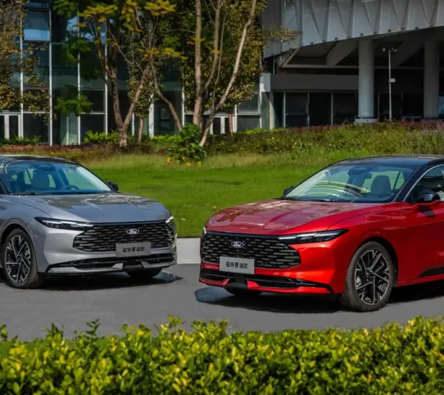 Dwa nowe Fordy Mondeo mk6, jeden czerwony, drugi szary, stoją obok siebie na tle nowoczesnego budynku i zieleni.
