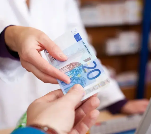 Eine Person in einem weißen Kittel reicht einen 20-Euro-Schein. Möglicherweise zur Bezahlung von Krankengymnastik Kosten.
