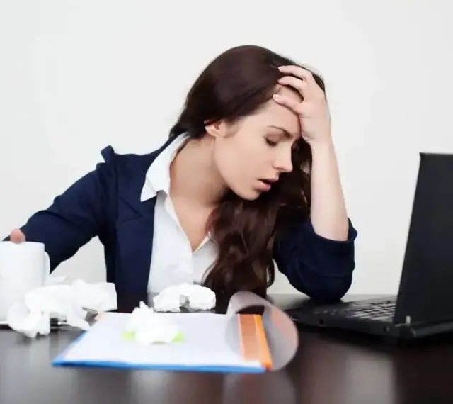 Zmęczona kobieta z kubkiem i chusteczkami przy laptopie. Zastanawia się, ile można być na zwolnieniu lekarskim od psychiatry.