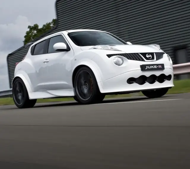 Biały Nissan Juke-R pędzi po torze, jego sportowy wygląd podkreślają szerokie nadkola i agresywny przedni zderzak.