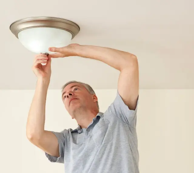 Mężczyzna wymienia żarówkę w lampie sufitowej, wykonując retrofit LED.