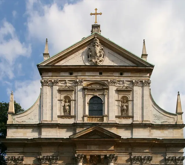 Bogata fasada kościoła w stylu barokowym, z rzeźbami i zdobieniami, pod błękitnym niebem.