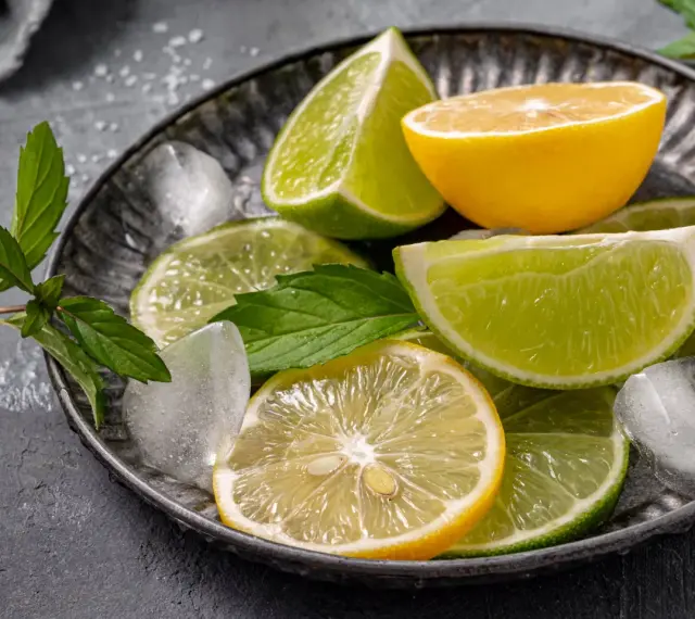 Plasterki cytryny i limonki, kostki lodu i listki mięty na metalowej tacy. Orzeźwiający zapach cytrusów, w tym limonen, unosi się w powietrzu.