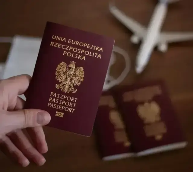 Dłoń trzyma polski paszport. Obok leżą kolejne dokumenty, maseczka i samolot. Czas oczekiwania na paszport wydłuża się.