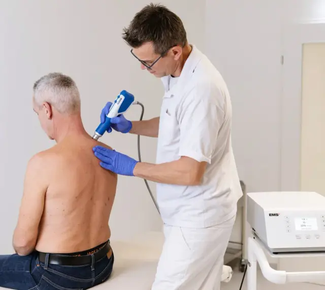 Therapeut behandelt Manns Schulter mit Stoßwellentherapiegerät. Es tut nicht weh, wie eine Spritze in die Schulter.