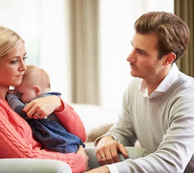 Zmartwiona mama tuli dziecko, a ojciec patrzy z troską. Czy to baby blues? Co to za uczucie?