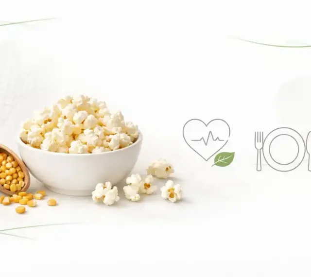 Misternie przygotowany popcorn w misce, obok ziaren kukurydzy na drewnianej łyżce. Czy popcorn tuczy? Ikony serca i talerza sugerują zdrowy wybór.