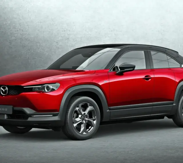 Czerwona Mazda MX-30 z czarnym dachem prezentuje się stylowo na tle szarej ściany.