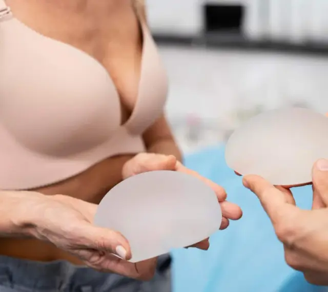 Dwie osoby trzymają implanty piersi. Kobieta w biustonoszu przygląda się implantom, które mogą być związane z przykurczem torebki implantu.