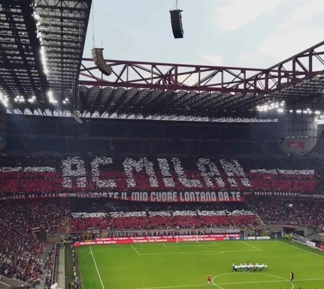 Trybuna stadionu San Siro w Mediolanie wypełniona kibicami AC Milan, tworzącymi napis "AC MILAN" i transparent "FOSSI DEI LEONI, VECCHIESTE IL MIO CUORE LONTANO DA TE".