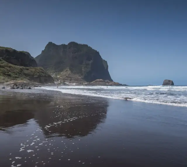 Dziecko bawi się na czarnej plaży Madera, w tle widać skaliste klify i ocean.