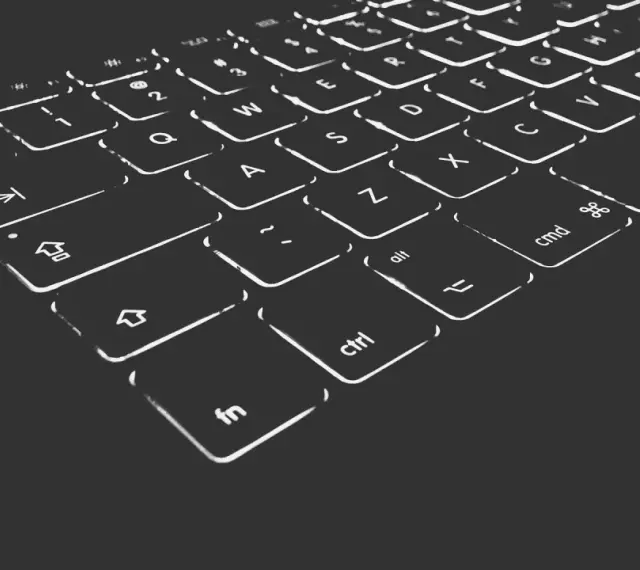 Nahaufnahme einer beleuchteten Tastatur. Die Tasten sind mit weißen Symbolen und Buchstaben versehen, die im Dunkeln leuchten. Die "Umschalt"-Taste ist deutlich zu erkennen.
