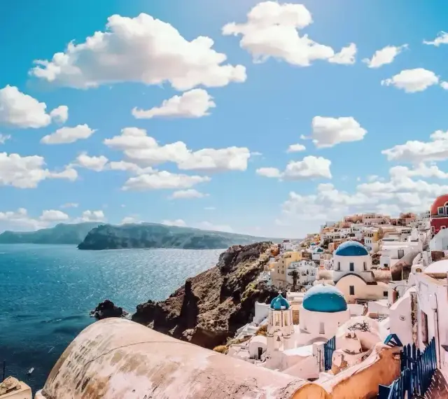 Santorini, Grecja. Białe domy z niebieskimi kopułami na klifie nad morzem. Zastanawiasz się, ile się leci do Grecji?