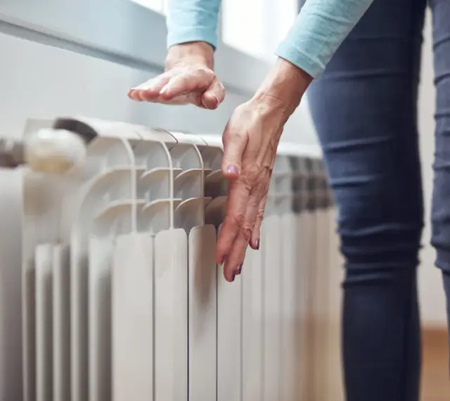 Dłonie sprawdzają temperaturę grzejnika, zastanawiając się, dlaczego grzejnik jest zimny na dole.