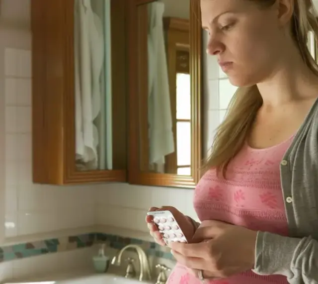 Zmartwiona ciężarna kobieta trzyma blister tabletek. Czy amoksycylina w ciąży jest bezpieczna?